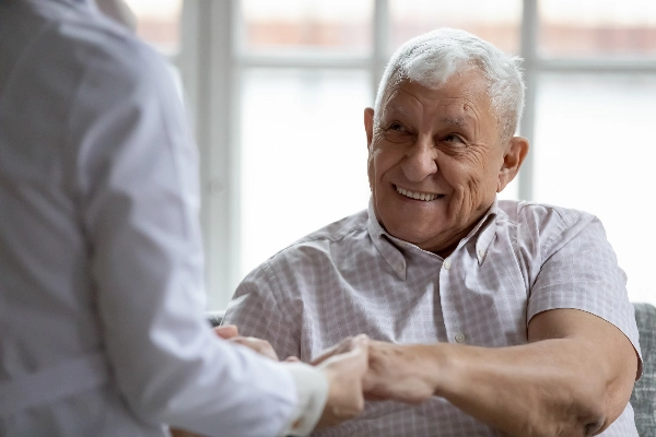A happy elderly man sitting and holding hands with his doctor.