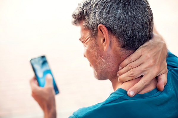 Gray-haired man has neck pain using his smartphone.
